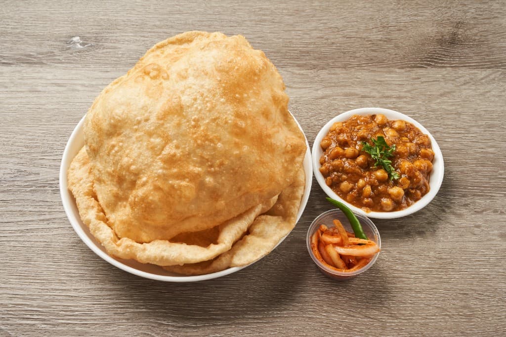 Chole bhature with puffed bhatura, chickpea curry, and pickles on a wooden table